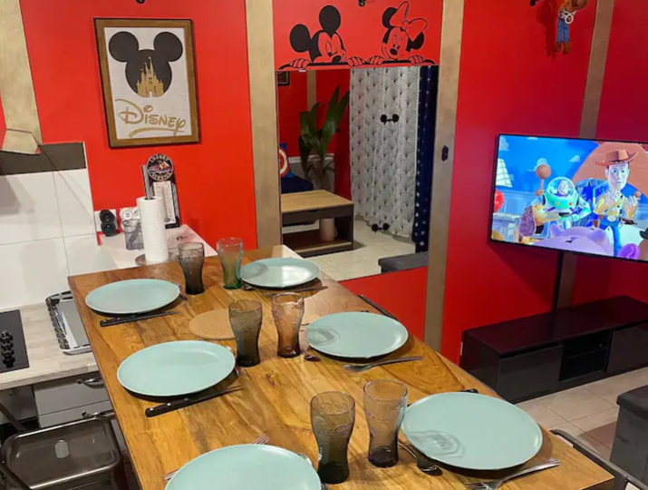 Salle à manger de la Disney Room. On y voit la table mise et une télé où est diffusé le film Toys Story. Le film se fond parfaitement dans le merveilleux décor de l'appartement.